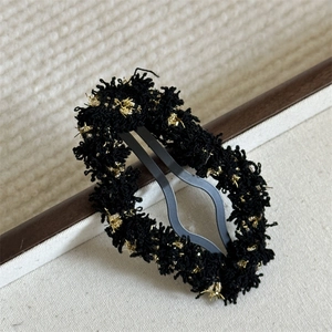 Detailed view of the black tweed fabric texture and gold metallic silk on the hair clip