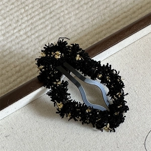 Close-up of black cloud yarn hair clip with golden silk detail on a wooden frame