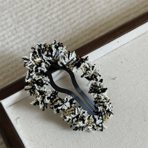 Close-up of elegant black and white tweed hair clip with gold metallic threads and metal base