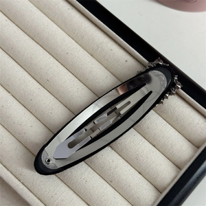 Detail view of water-drop BB hair clip with silver spring clasp on beige velvet display box