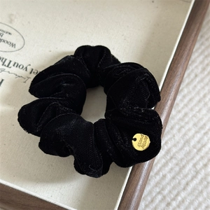 Close-up of black velvet scrunchie with a gold handmade charm and pleated details
