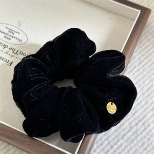 Close-up of black velvet scrunchie with vintage gold charm on fabric display tray