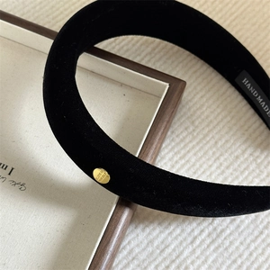 Detail of black velvet padded headband with gold metal disc and handmade woven label