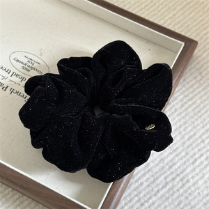 Macro shot of black velvet scrunchie with glitter and a small gold metal logo detail