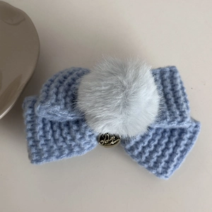Détail de pince à cheveux nœud tricoté bleu clair avec pompon gris et breloque dorée