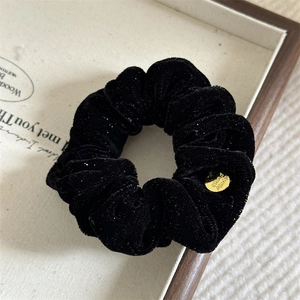 Detailed close-up of a black velvet scrunchie featuring a golden Hand Made metal charm