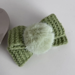 Détail d'un nœud à cheveux tricoté vert avec pompon doux sur fond blanc purifié