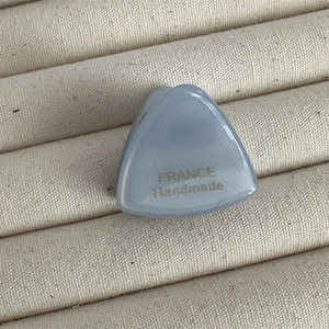 Gros plan sur une pince à cheveux triangle en acétate bleu-gris avec logo doré