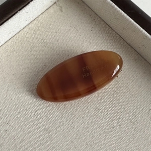 Detailed macro view of an oval acetate hair clip with amber texture and handmade engraving