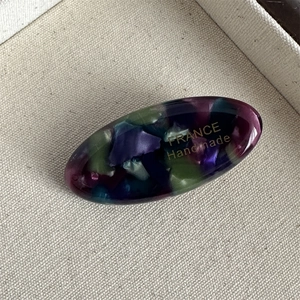 Detail of oval acetate hair clip with colorful resin patterns and golden France handmade text