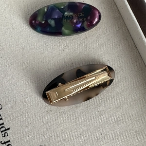 Detailed macro of oval acetate hair clips with golden metal duckbill mechanism and text