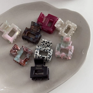 Collection of mini acetate hair claws with marble and leopard patterns in a ceramic tray