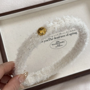 Detail eines weichen weißen Kunstpelz-Stirnbands mit goldener Smiley-Metallschnalle