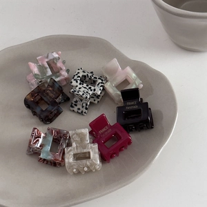 Close-up of small acetate hair claws with marble and leopard patterns in a ceramic tray