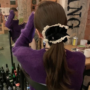 Detail of a large black velvet scrunchie with lace trim and metal pendant on hair