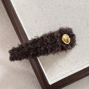 Nahaufnahme der dunkelbraunen Plüsch-Haarspange mit goldenem Smiley-Gesicht-Dekor