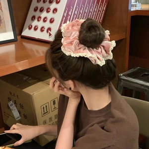 Detailed view of a pink velvet scrunchie with lace edge worn on a bun hairstyle
