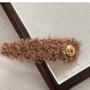 Detailansicht der braunen Plüsch-Haarklammer mit goldenem Metall-Smiley-Emblem