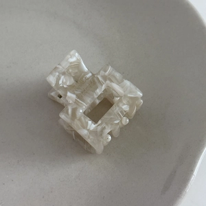 Macro view of square acetate hair claw clip with cream marble texture and metal spring detail