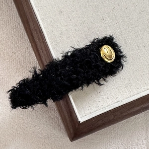 Detailaufnahme der schwarzen Plüsch-Haarspange mit goldener Smiley-Metallverzierung