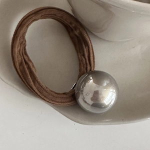 Detail of brown elastic hair tie with a polished silver sphere on white ceramic tray