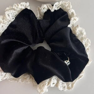 Close-up of black velvet hair scrunchie with white lace trim and small metal charm