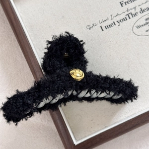 Detailaufnahme einer schwarzen Plüsch-Haarklammer mit einem goldenen Smiley-Metall-Emblem