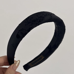 Detail of black satin headband featuring textured floral jacquard and padded structure
