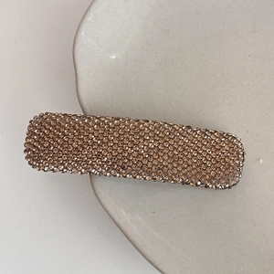 Close-up of a rectangular hair clip with gradient amber rhinestones on a ceramic dish