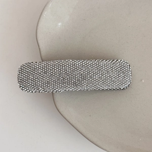 Close-up of a sparkling rectangular barrette with micro-set rhinestones on a ceramic dish