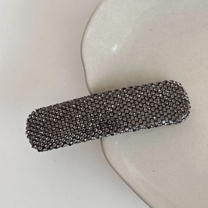 Close-up of rectangular hair clip with gray rhinestones on a ceramic plate edge