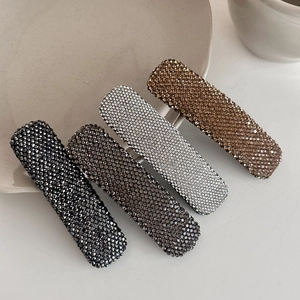 Detailed close-up of sparkling rhinestone hair clips in four elegant colors on a ceramic tray