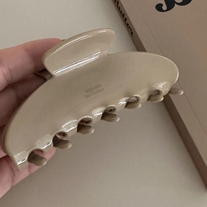 Dettaglio di una molletta per capelli in acetato beige lucido dal design semplice