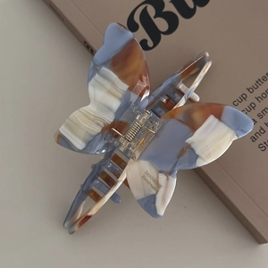 Detail view of acetate butterfly hair claw clip with blue marble pattern and gold spring