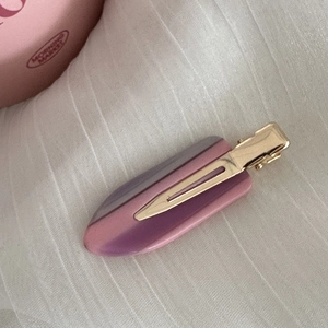 Macro d'une barrette en acétate rose-violet avec base dorée sur un tissu blanc doux