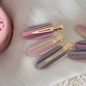 Vue détaillée de barrettes en acétate tons rose et violet sur un tissu en soie blanc