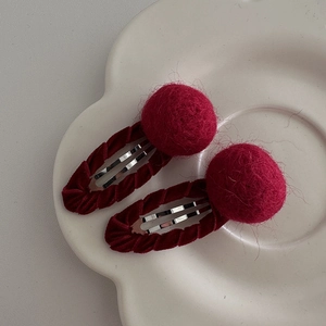 Close-up of a pair of festive red faux fur pom-pom BB hair clips on a white plate