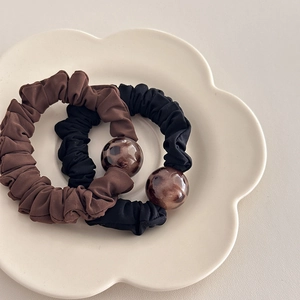Close-up of leopard pattern beads and pleated fabric hair ties on a white ceramic plate