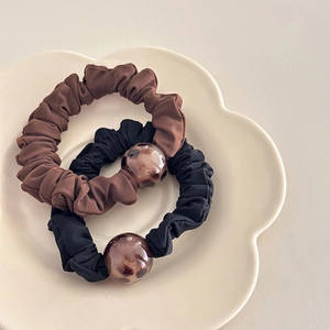 Two-pack leopard print bead scrunchies in black and brown colors on floral tray