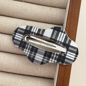 Macro detail of wave-shaped black and white plaid hair clip on a beige velvet tray