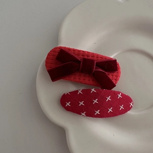 Detail view of red velvet bow hair clips and woven fabric hairpins on a white ceramic tray