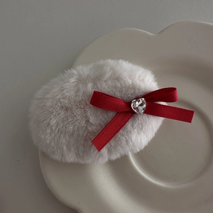 Close-up of a plush cream hair clip with a red ribbon bow and heart-shaped crystal detail