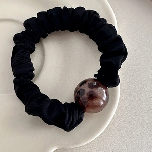 Detail of black pleated scrunchie with a brown leopard print bead on ceramic plate