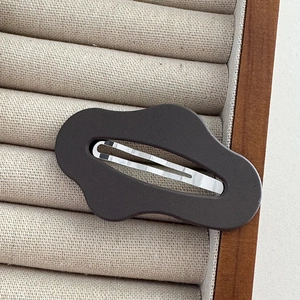Close-up of matte coffee brown wavy hair clip with metal spring on beige velvet