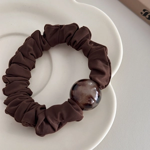 Detail shot of a dark brown ruffled scrunchie with a tortoise shell resin bead on a white plate