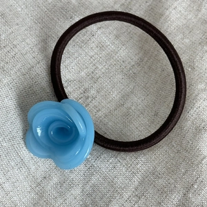 Dettaglio di un fiore di rosa in acetato blu su un elastico per capelli marrone