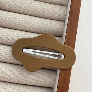 Detail view of a brown wavy hair clip on beige velvet display with wooden frame