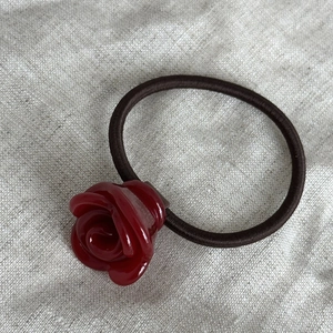 Dettaglio macro dell'elastico per capelli con rosa rossa in acetato lucido su lino