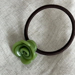 Dettaglio di un elastico per capelli con rosa verde su uno sfondo grigio testurizzato