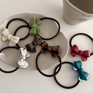 Handmade acetate bow hair ties in seven assorted colors on a beige ceramic plate